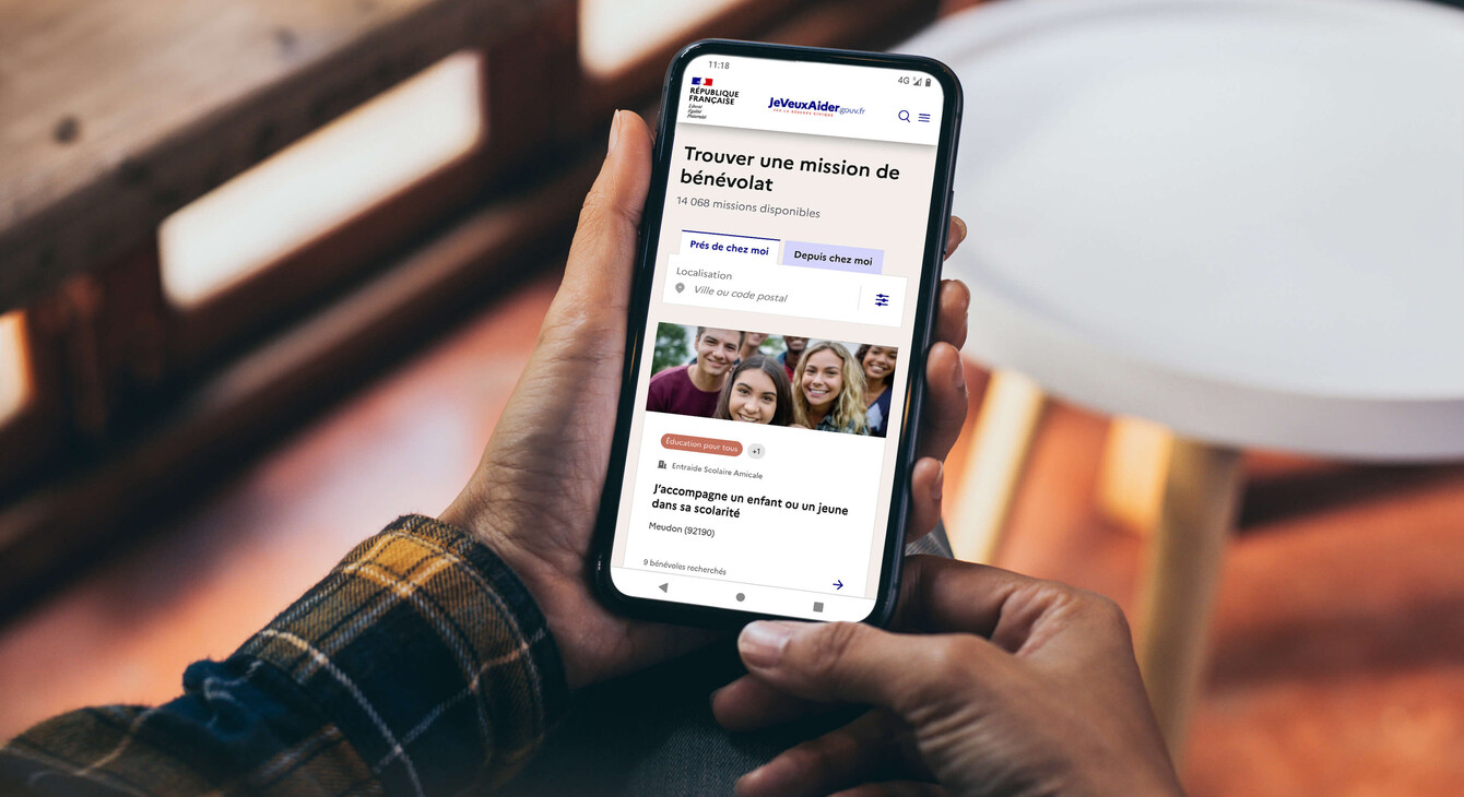 Image d'une personne tenant un téléphone qui affiche la page des missions du site jeveuxaider.fr