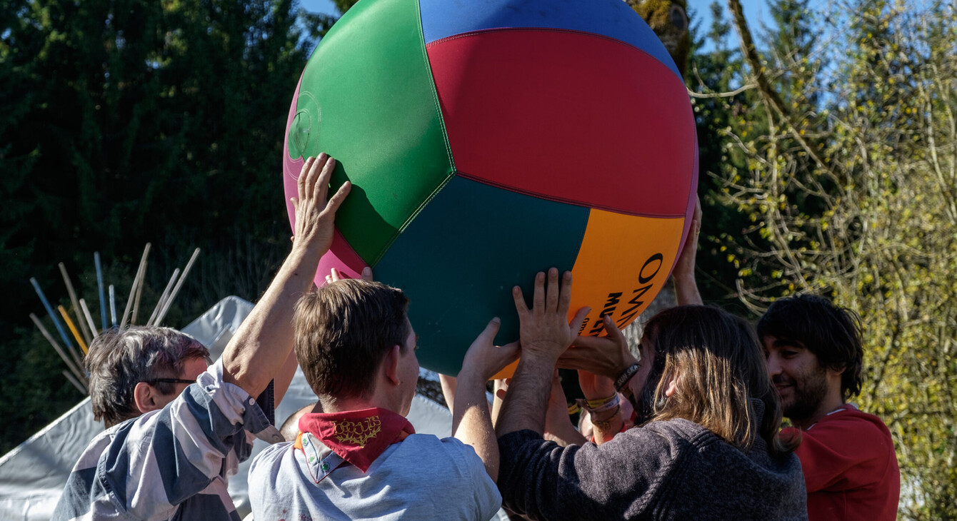 Des personnes tiennent une balle géante à plusieurs, jouant ainsi au kin-ball, dans un cadre ludique